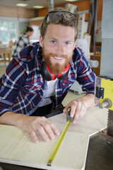 smiling young man measuring wooden board