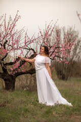 Woman peach blossom. Happy woman in white dress walking in the garden of blossoming peach trees in spring