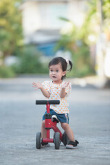 Cute Asian baby girl sitting on a red bicycle for children.