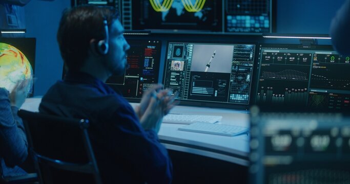 Diverse Flight Control Operators In Headsets Monitor Space Mission On Computers In Mission Control Center. Team Clap Hands After Successful Space Rocket Launch Displayed On Big Digital Screens.