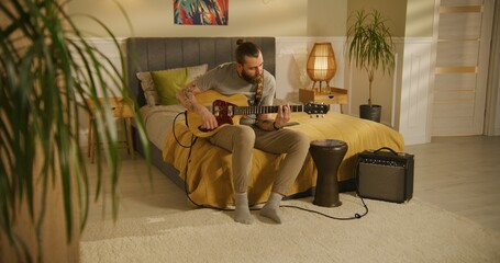 Man plays guitar in bedroom.