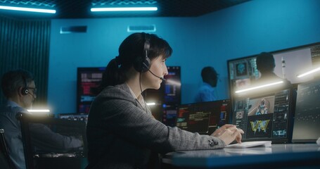 Female flight control worker in headset sits in front of computer, monitors space mission in mission control center, looks at camera. Team watch space rocket lift off on big digital screens. Portrait. - Powered by Adobe
