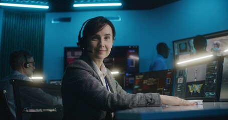 Female flight control worker in headset sits in front of computer, monitors space mission in mission control center, looks at camera. Team watch space rocket lift off on big digital screens. Portrait. - Powered by Adobe