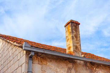 Old brick chimney on the roof of a house against the blue sky . Wall are made up of rectangular...