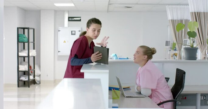 Caucasian female doctor talking to medical recepcionist at front desk at hospital, slow motion