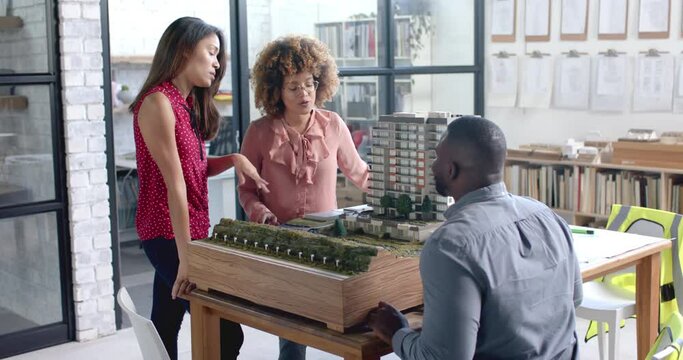Busy diverse colleagues discussing work over city model on table in office in slow motion