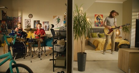Man plays guitar in bedroom. Young boy plays drum kit and young girl plays ukulele, jumps on bed. View of two rooms or apartments separated by wall. Concept of music, neighbourhood and lifestyle.