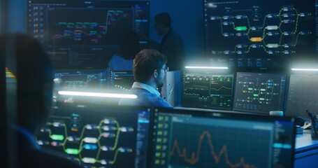 Technical support specialist types keyboard sitting at computer with displayed blockchain network map and server data. Big data scientists work in monitoring room late night. Cyber security concept.