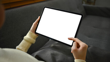Closeup shot of young woman sitting on couch and using digital tablet. White empty screen for your advertising text message
