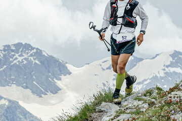athlete runner running mountain trail skyrunning race on edge of cliff, trekking poles in hand