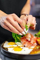 woman chef hand cooking fried eggs with ham, salad and hummus