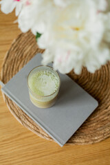 Home cozy interior. A bouquet of peonies in a glass vase, a glass of matchalate on a wooden coffee table. Spring.