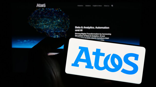 Stuttgart, Germany - 06-17-2023: Person holding cellphone with logo of French information technology company Atos SE on screen in front of webpage. Focus on phone display.