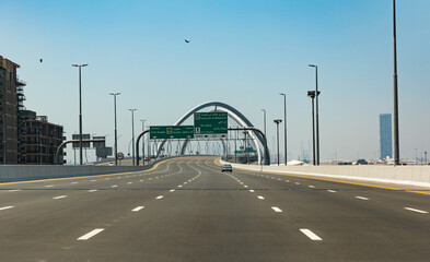 Dubai, United Arab Emirates - April 21th 2023: Empty Infinity Bridge road with only one car. Direction Port Rashid and Dubai down town. Blue sky with birds. Infinity Bridge behind the road sign.