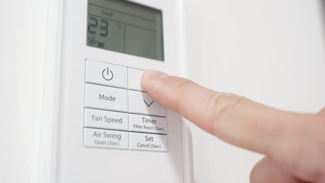 The camera focuses closely on the white air conditioner remote control as the man increases the temperature using his finger.