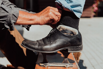 An old man hand polishing and painting a black shoe at street