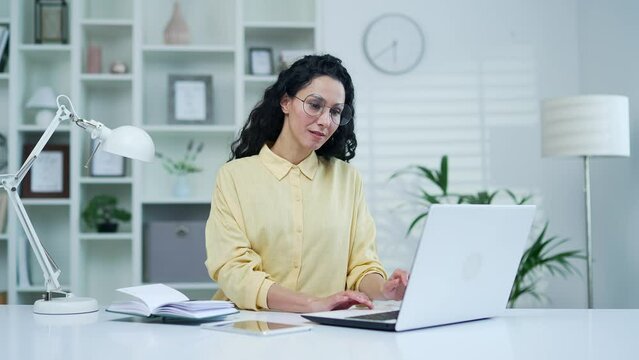 Young brunette businesswoman typing on laptop while sitting in home office. Female freelancer works on a computer on a project, chats online with a client, writes an email message, shopping online 