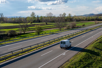 White modern delivery small shipment cargo courier van moving fast on motorway road to city urban suburb. 