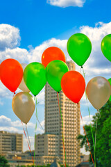 Helium balloons of various colors with buildings in the background.