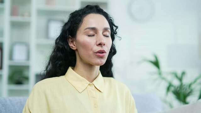 Close up of a young brunette woman relaxing with her eyes closed while sitting in the living room. Portrait of a calm happy female resting after work breathing deeply at home. Meditation concept