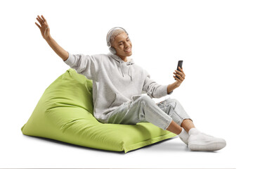 African american young man seated on a bean bag and listening to music from a mobile phone