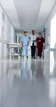 Vertical video of diverse doctors using tablet and walking in corridor at hospital, slow motion