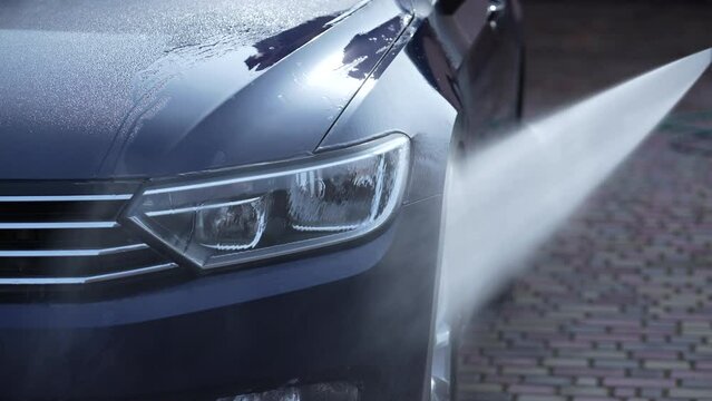 Washing a blue car with high pressure water cleaner, outdoors, close up