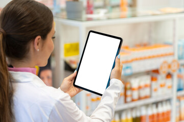 Female pharmacist looking at the screen of a digital tablet in the pharmacy - obrazy, fototapety, plakaty