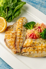 Grilled sea bream fillet with vegetables and greens on wooden table