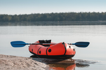 Red packraft with a paddle on the seashore.