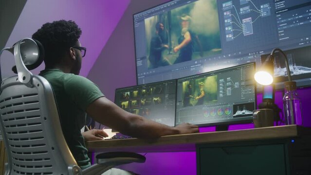 African American video editor makes color grading, works at home office. Computer and big digital screen with program interface with RGB tools and action movie footage. Film post production concept.
