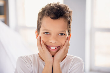 Photo of pretty dreamy little boy dressed white t-shirt smiling arms cheeks indoors house home room