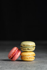 Colorful macaroons stacked in a pile on a grey table, black background