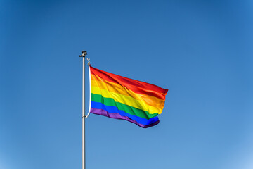 The rainbow flag of the LGBTQ community flies against blue clear sky