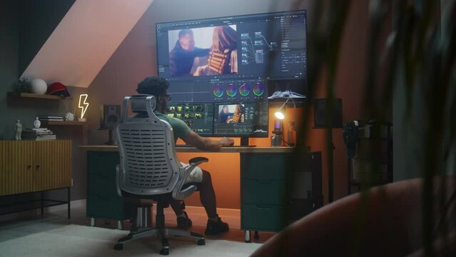 African American colorist edits action movie, makes color correction in professional software on multi-monitor computer and big digital screen, works at home office. Concept of film post production.