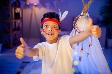 Photo of joyful surprised boy in native american costume have theme party birthday thumb up symbol in evening playroom