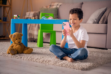 Photo of cute sweet boy have free time after elementary school using device playing web games in nursery room