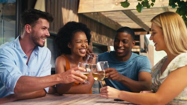 Smiling group of multi-cultural friends outdoors on holiday or at home drinking wine and doing cheers together  - shot in slow motion