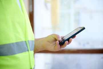 Engineer with white helmet using his smart phone at the construction site. Portrait of mature...