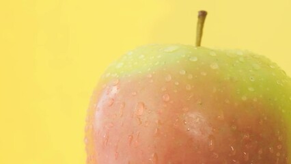 Macro video of a large apple in water drops rotating on a yellow background.  - Powered by Adobe