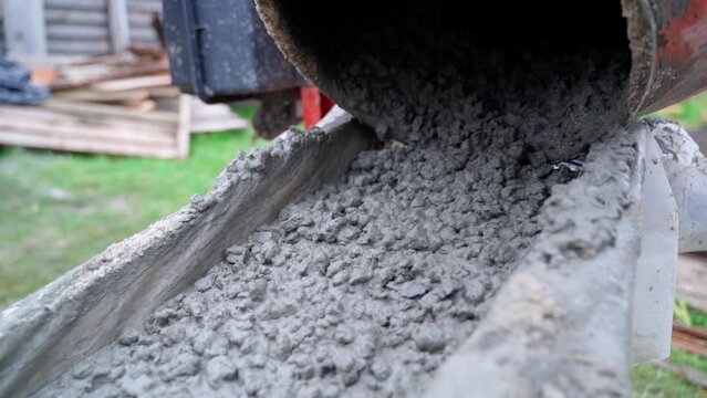 Thick concrete mortar flows down from the concrete mixer close-up in slow motion