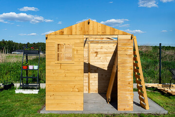 A wooden garden shed under construction standing on a concrete foundation in the garden.