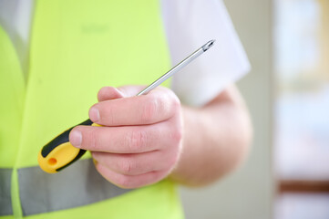 Cropped view of construction worker using screwdriver during work. Electrician in uniform using his instruments at the construction site. Close up view.