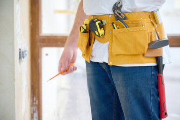 Cropped view of the electrician with a screwdriver in his hand wearing in white T-shirt and blue...