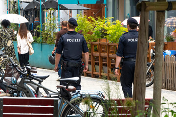 Two Austrian police officers patrol a pedestrian street in downtown Vienna, view from the back.