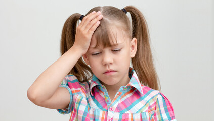 Child with headache holding hand on head on white background caucasian little girl 6-7 years looking down