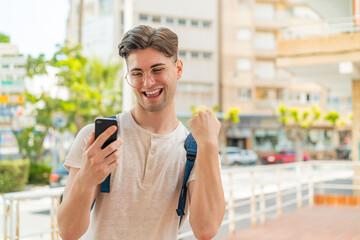 Young handsome man using mobile phone at outdoors celebrating a victory