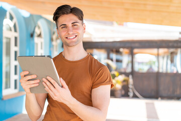 Young handsome man holding a tablet at outdoors smiling a lot