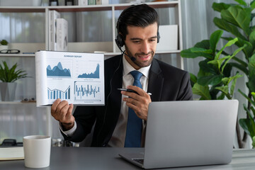 Business man wearing headphone present financial data or BI paper via laptop during online meeting....