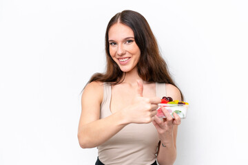 Young caucasian woman holding a bowl of fruit isolated on white background giving a thumbs up gesture